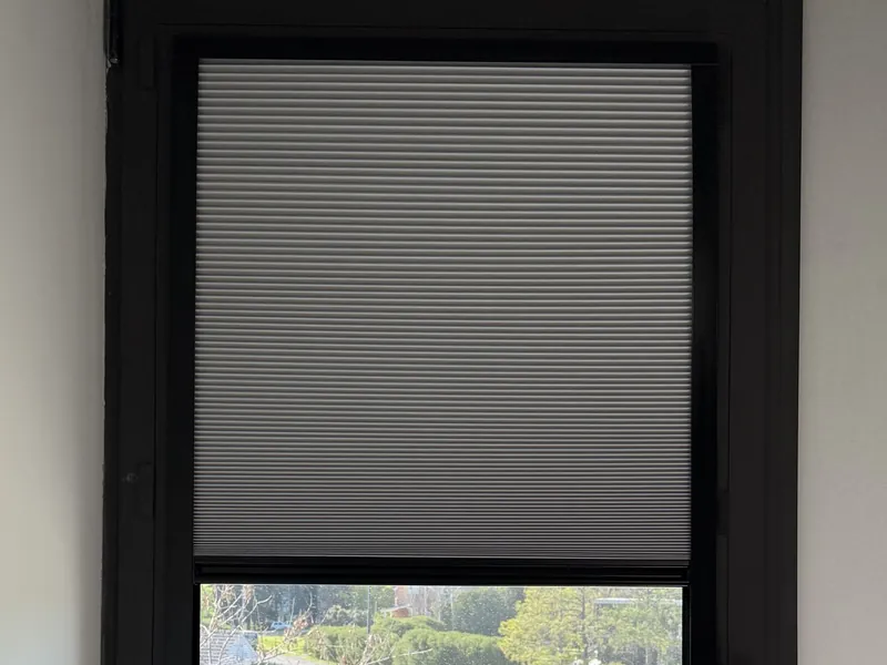 Cortina celular gris en una ventana alta de aluminio negro, a medio subir