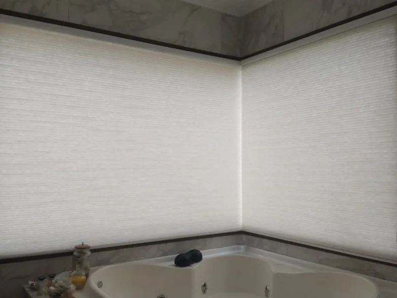 Cortinas celulares translúcidas blancas en un ventanal en esquina, con la luz del día atravesando la tela